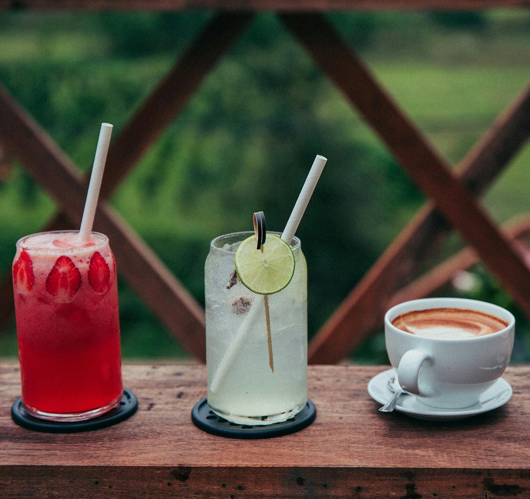 Assortment of beverages including coffee and fruity drinks on a wooden table outdoors.