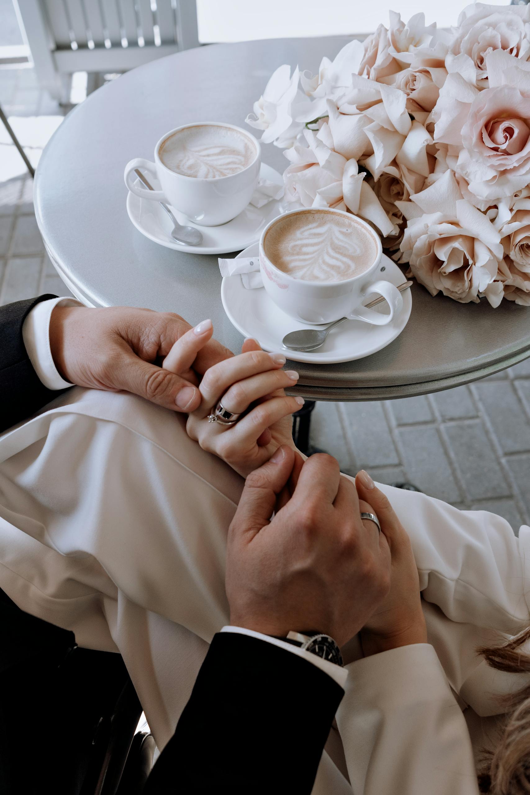 Elegant moment of a newlywed couple holding hands with coffee and roses on a table.