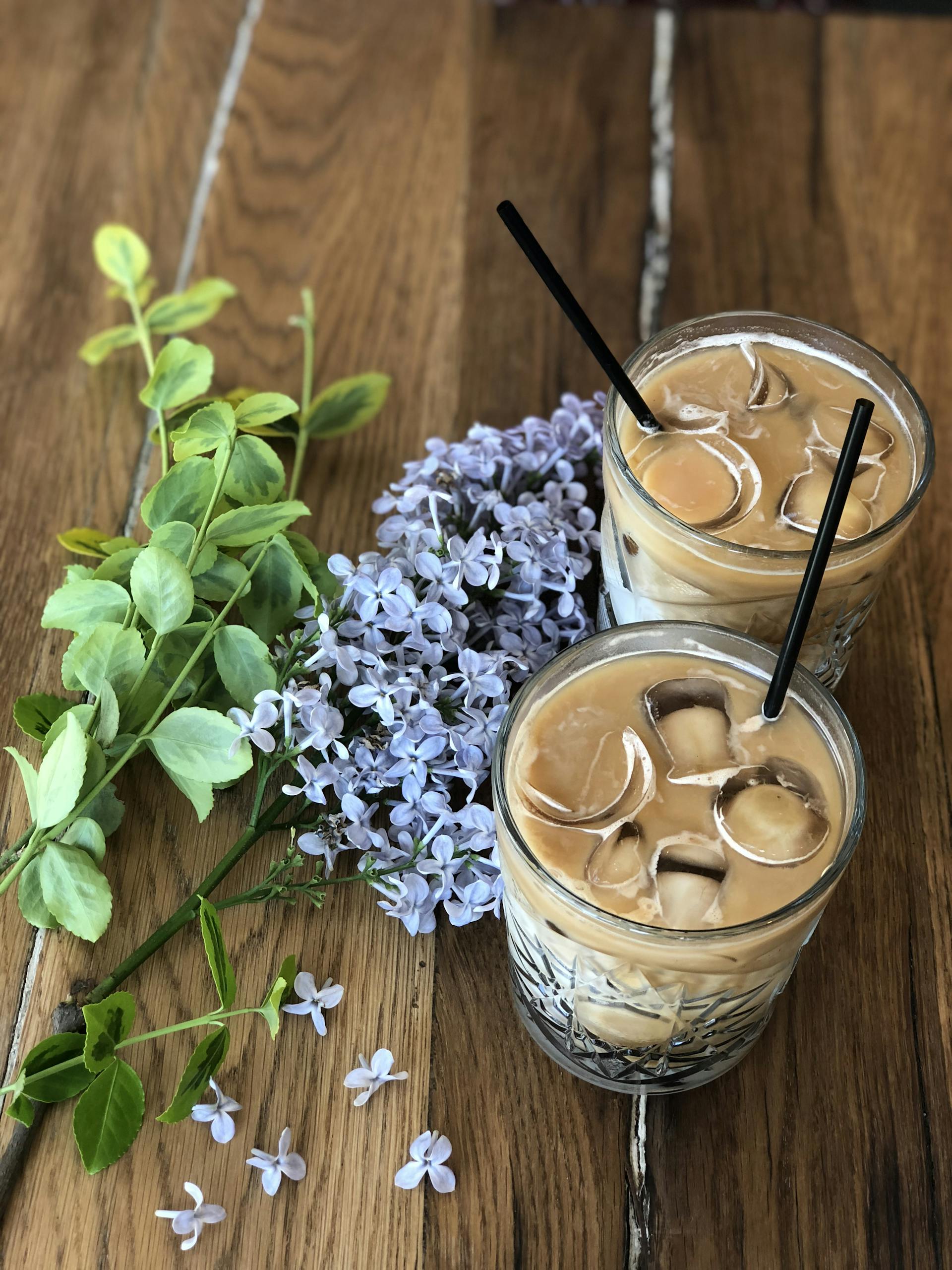 Two glasses of iced coffee with lilac flowers on a wooden table. Perfect for a summer refreshment.